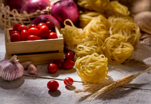 Pasta fettuccine sobre mesa de madera con tomates cherry y huevos en segundo plano.