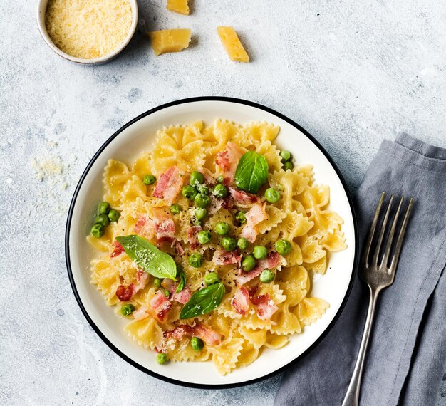 Pasta fettuccine con tocino y guisantes y queso parmesano en placa de luz sobre fondo de hormigón gris antiguo. Vista superior.