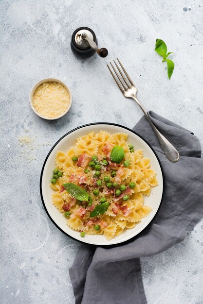 Pasta fettuccine con tocino y guisantes y queso parmesano en placa de luz sobre la superficie de hormigón gris antiguo