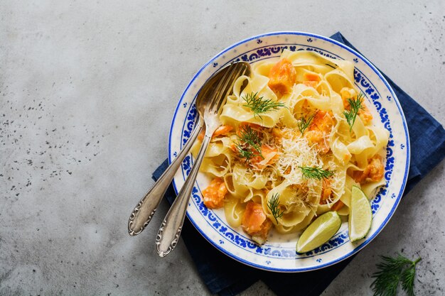 Pasta fettucine con salmón y queso parmesano en salsa cremosa en placa de cerámica sobre superficie de hormigón gris antiguo