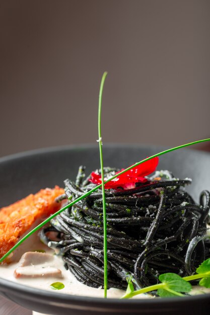 Pasta fresca de tagliolini negro con pollo en hierbas sobre rúcula y tomate