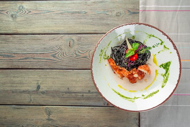 Pasta fresca de tagliolini negro con pollo en hierbas sobre rúcula y tomate