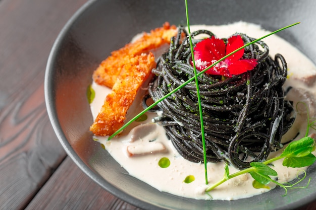 Pasta fresca de tagliolini negro con pollo en hierbas sobre rúcula y tomate