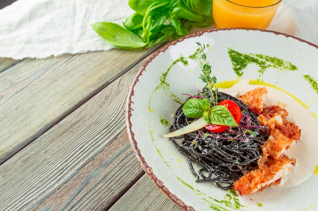 Pasta fresca de tagliolini negro con pollo en hierbas sobre rúcula y tomate