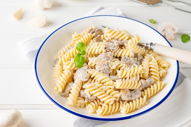 Pasta fusilli con champiñones, queso y albahaca fresca en un plato sobre un fondo blanco de madera