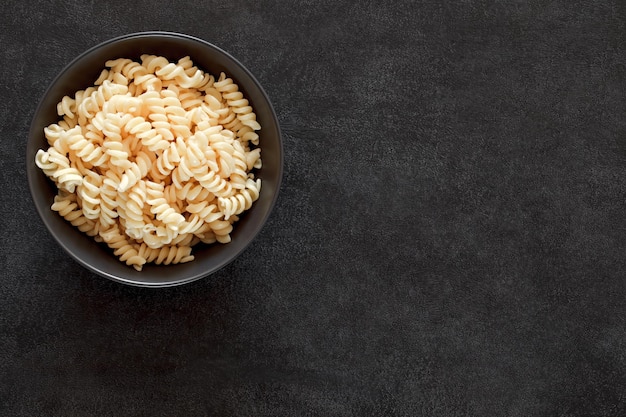 Pasta fusilli cocida en un tazón en el espacio de vista superior de fondo oscuro para copiar texto