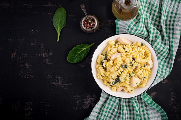 Pasta Fusilli com um molho cremoso com carne de frango, queijo parmesano e espinafre em uma tigela em um fundo escuro