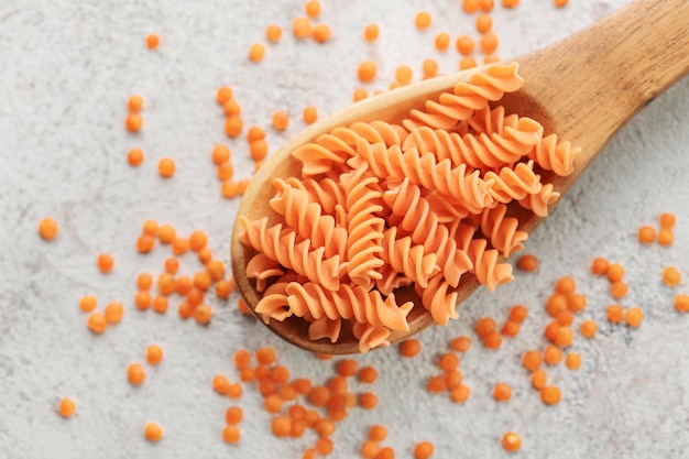 Pasta fusilli de lentejas rojas sobre un fondo de hormigón gris Cuchara con pasta cruda y lentejas rojas Pasta sin gluten