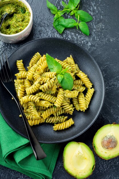 Pasta Fusilli mit grüner Avocado-Basilikum-Sauce und Zutaten auf schwarzem Tisch. Draufsicht. Speicherplatz kopieren.