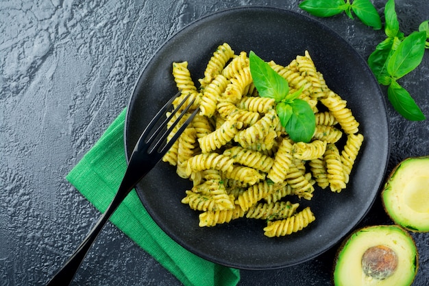 Pasta Fusilli con salsa de albahaca de aguacate verde e ingredientes en mesa negra. Vista superior. Copie el espacio.