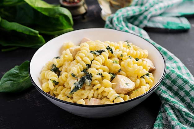 Pasta de fusilli con una salsa cremosa con carne de pollo, queso parmesano y espinacas en un cuenco sobre un fondo oscuro