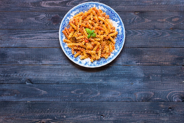 Pasta fusilli con salsa de tomate, tomate, cebolla, ajo, pimentón seco, aceitunas, pimiento y aceite de oliva, sobre un fondo de madera.