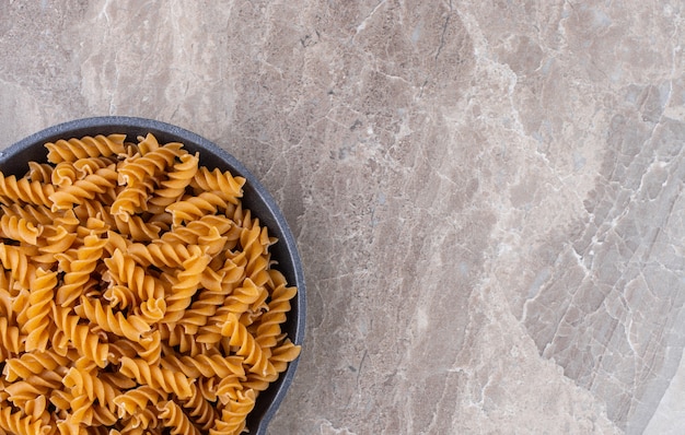 Pasta fusilli en una sartén, sobre el mármol.