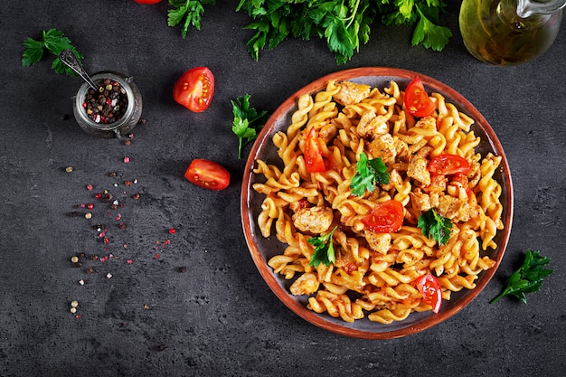 Pasta fusilli con tomate, carne de pollo y perejil en un plato sobre la mesa oscura