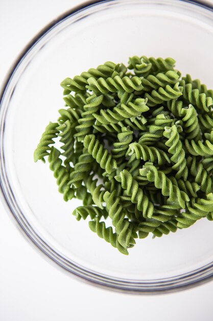 Pasta fusilli verde cruda en plato transparente, natural a base de espinacas y espirulina. Comida deliciosa y saludable. De cerca.