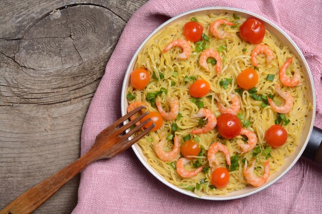 Foto pasta con gambas y tomate sobre fondo de madera