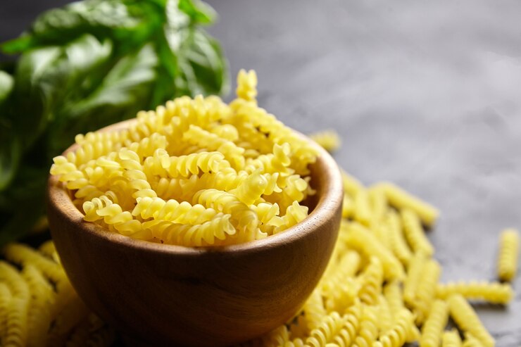 Pasta Girandole en cuenco de madera y hierba de albahaca verde sobre mesa de piedra negra