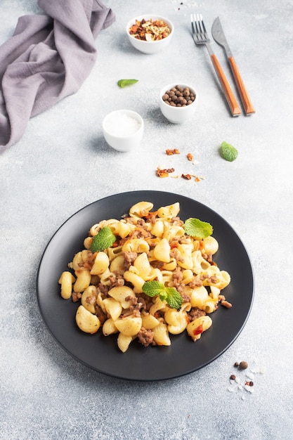 Pasta guisada con carne picada y verduras, macarrones a la Marina en un plato. Fondo de hormigón gris. Copie el espacio.