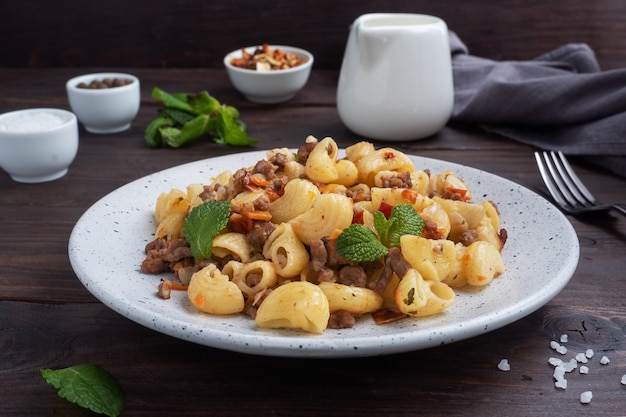 Pasta guisada con carne picada y verduras, macarrones a la Marina en un plato. Fondo de madera oscura.