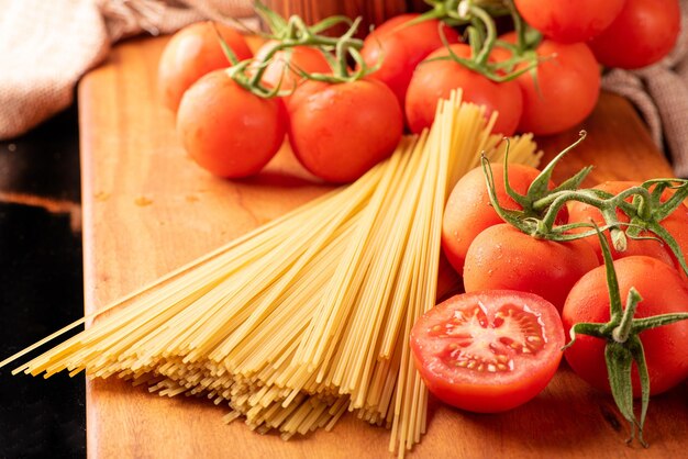 Pasta hermosos detalles de tomates rojos y hebras de espaguetis crudos sobre enfoque selectivo de madera rústica