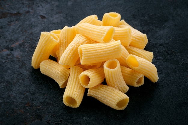 Foto pasta de huevo rigatoni cruda dorada sobre un fondo de piedra oscura. tipo de pasta italiana, cerrar