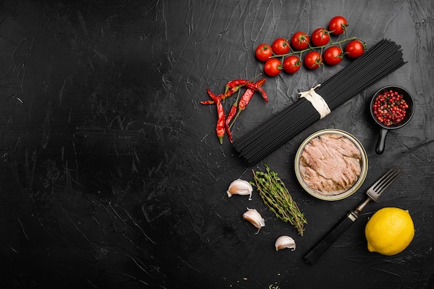 Pasta con ingredientes crudos de atún, sobre fondo de mesa de piedra oscura negra, vista superior plana, con espacio para copiar texto