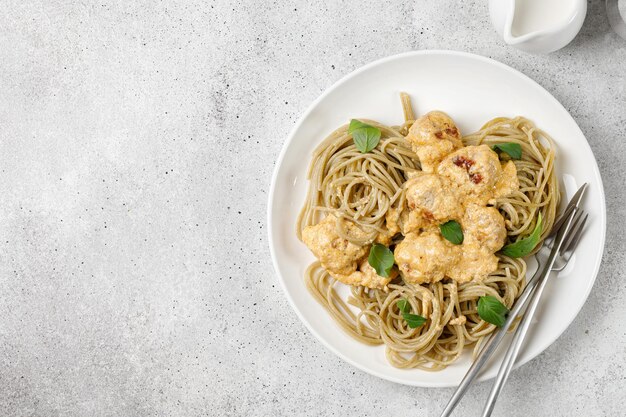 Pasta integral con albóndigas con salsa de crema y verduras sobre fondo gris plato blanco