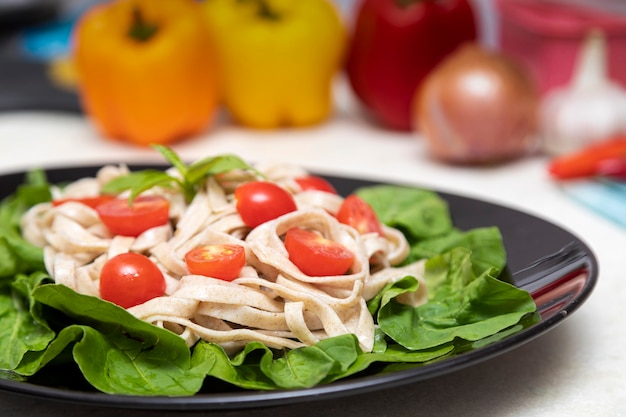 Pasta integral con hojas verdes de rúcula y tomate cherry sobre placa negra y fondo de mármol blanco