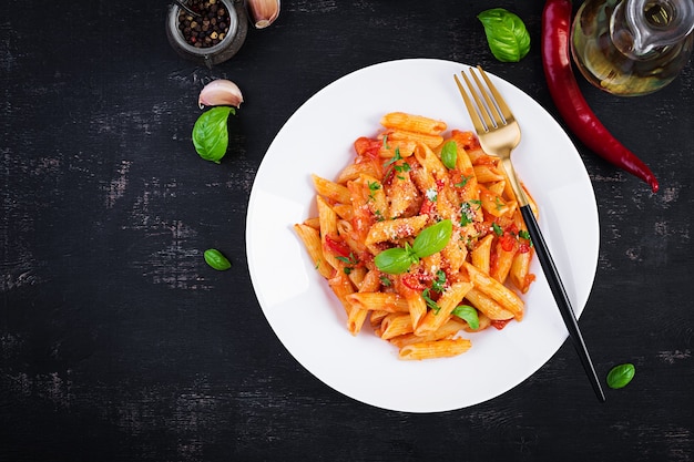 Pasta italiana clásica penne alla arrabiata con albahaca y queso parmesano recién rallado en mesa oscura. Pasta penne con salsa de chile arrabbiata. Vista superior, arriba, espacio de copia