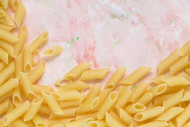 Foto pasta italiana cruda de penne sobre un fondo rosado