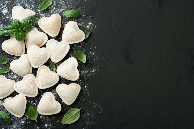 Pasta italiana de ravioli em forma de coração saborosa ravioli crua com farinha e manjericão em fundo escuro Ingredientes de culinária de fundo Ideias de almoço de Dia dos Namorados ou Dia das Mães Vista superior com espaço de cópia