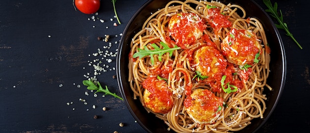 Pasta italiana. Espaguetis con albóndigas y queso parmesano en placa negra sobre fondo oscuro de madera rústica. Cena. Vista superior. Concepto de comida lenta