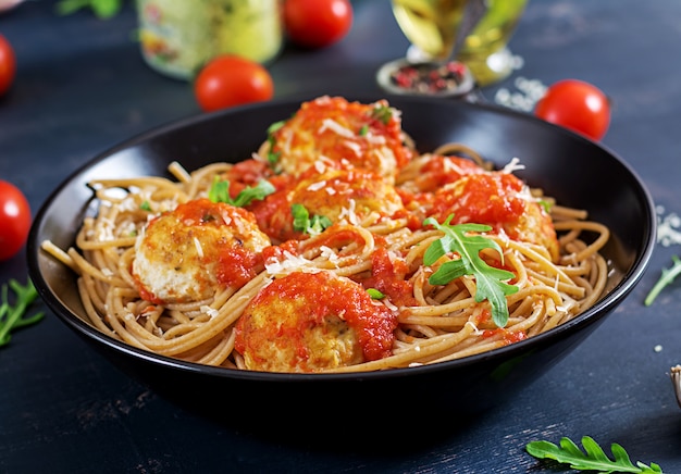 Pasta italiana. Espaguetis con albóndigas y queso parmesano en plato negro sobre la mesa de madera rústica oscura. Cena. Concepto de comida lenta