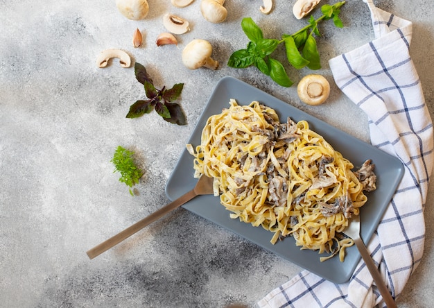 Pasta italiana fettuccine casera con champiñones y salsa de crema servida en un plato gris con albahaca (Fettuccine al Funghi Porcini). Cocina tradicional italiana. Fondo gris, vista superior, espacio de copia