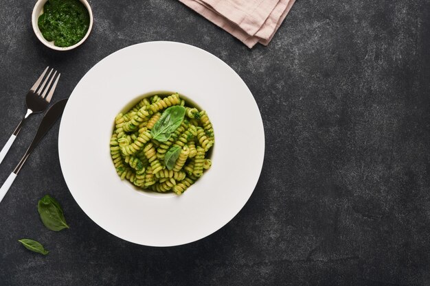 Pasta italiana Fusilli con pesto Pasta fusilli con pesto de albahaca y hierbas queso parmesano albahaca y ajo en plato blanco sobre fondo de encimera de piedra negra Vista superior Copiar espacio Maqueta