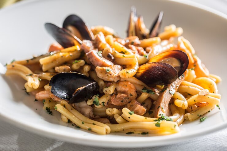 Pasta italiana con mejillones y gambas en plato blanco.