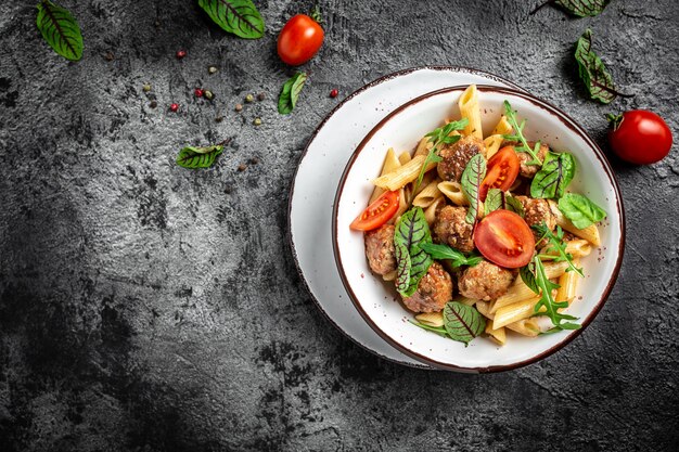 Pasta italiana. Pasta penne con albóndigas en salsa de tomate en un recipiente artesanal blanco sobre una superficie de piedra gris