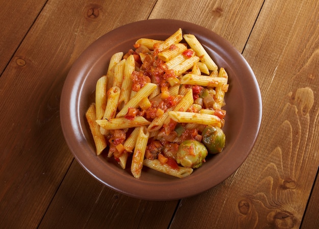 Pasta italiana Penne rigate con salsa de tomate vegetal sobre mesa de madera