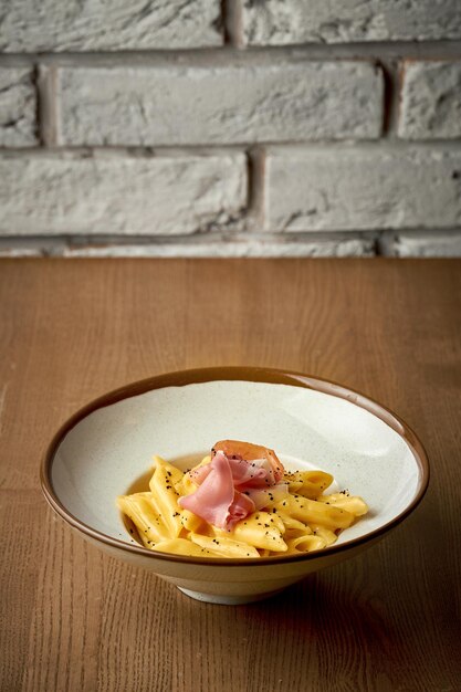 Pasta italiana con salsa de queso y jamón en un plato sobre un fondo de madera