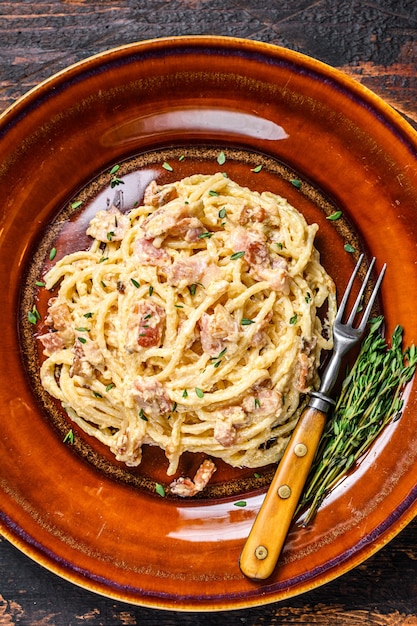 Pasta italiana Spaghetti Carbonara con tocino, queso parmesano duro y salsa de crema. Mesa de madera oscura. vista superior.