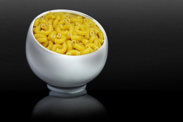 Pasta italiana en taza de porcelana. Pasta en forma de cuerno. Fondo negro. Concepto publicitario con espacio de copia de texto personalizado.