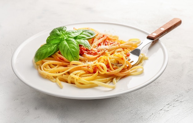 Pasta italiana con tomate, queso parmesano y albahaca en un plato blanco sobre blanco.