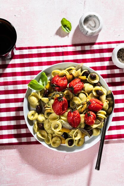 Foto pasta italiana de verano orecchiette con tomates al horno, aceitunas y pesto sobre fondo rosa