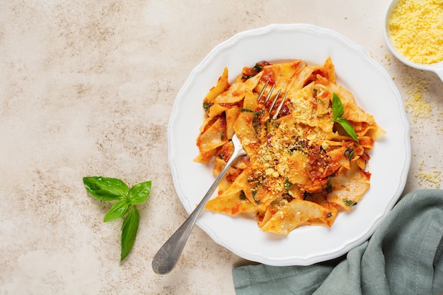 Pasta Maltagliati mit klassischer Tomatensauce, Parmesan und Basilikum auf einem rustikalen Betonleuchttischhintergrund. Traditionelles italienisches Gericht. Draufsicht.