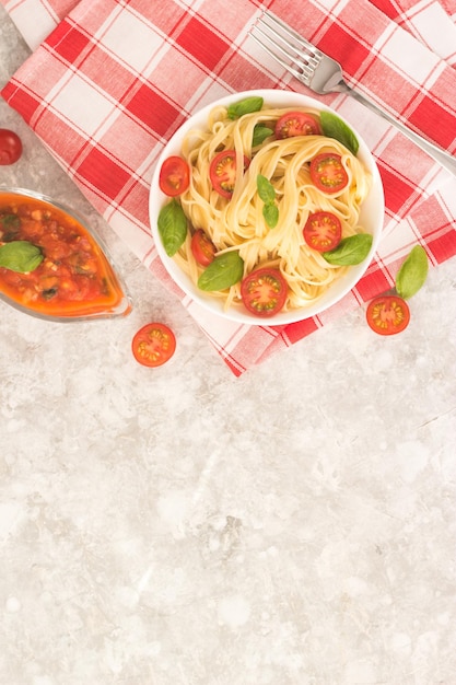 Pasta marinara en un plato blanco sobre una mesa blanca con rodajas de tomate y hojas de albahaca.