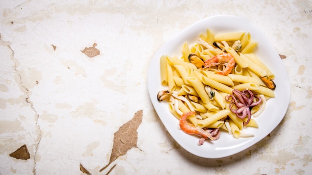 Pasta con mariscos y camarones en un plato blanco. Sobre mesa rústica. Espacio libre para texto. Vista superior