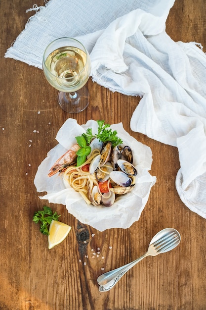 Foto pasta con mariscos. espaguetis con almejas y camarones en un tazón, copa de vino blanco sobre mesa de madera rústica