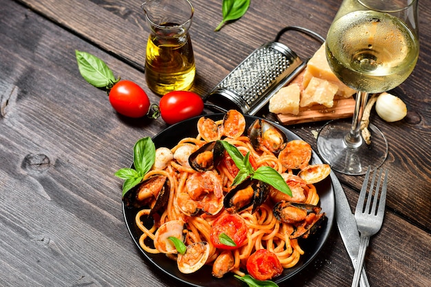 Foto pasta de mariscos espaguetis con almejas y langostinos con mejillones y tomates en un plato blanco con sobre una mesa de madera. receta de cocina italiana. vista superior