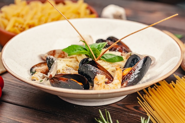 Pasta de mariscos con mejillones y albahaca en placa sobre mesa de madera