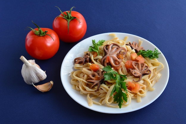 pasta con mariscos y tomates en el plato blanco sobre el fondo azul oscuro